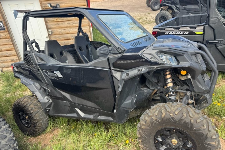 Black off-road vehicle parked on grass near a wooden building.