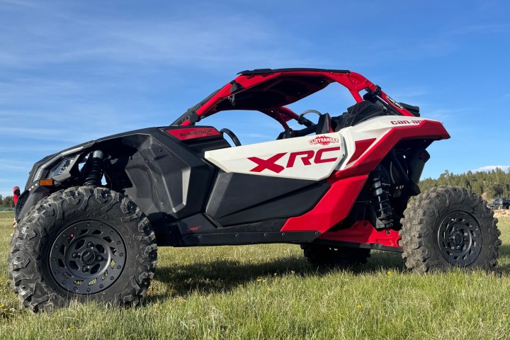 Red and white XRC off-road vehicle parked on grass under blue sky.