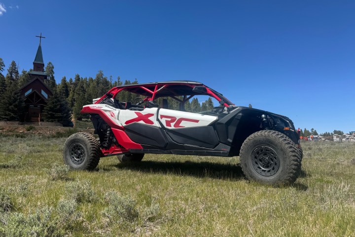 Red and white off-road vehicle in grassy field near a small church.