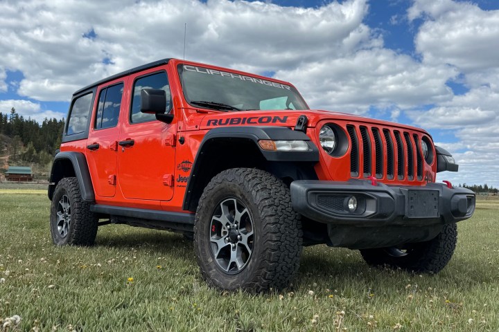 Red Jeep Wrangler Rubicon parked on grass under cloudy sky.