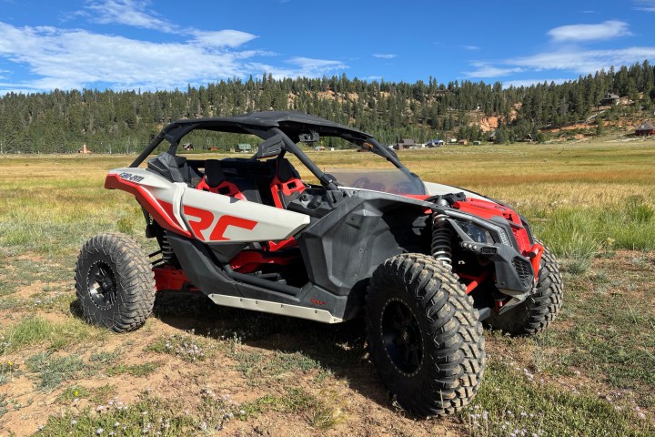 Off-road vehicle on grassy field with trees and blue sky in background.