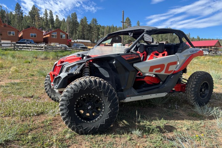 Off-road vehicle on grass with wooden cabins in the background.